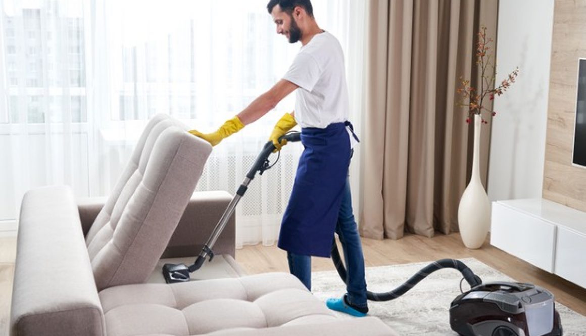 young-man-cleaning-sofa-with-vacuum-cleaner-leaving-room-home_130111-3594